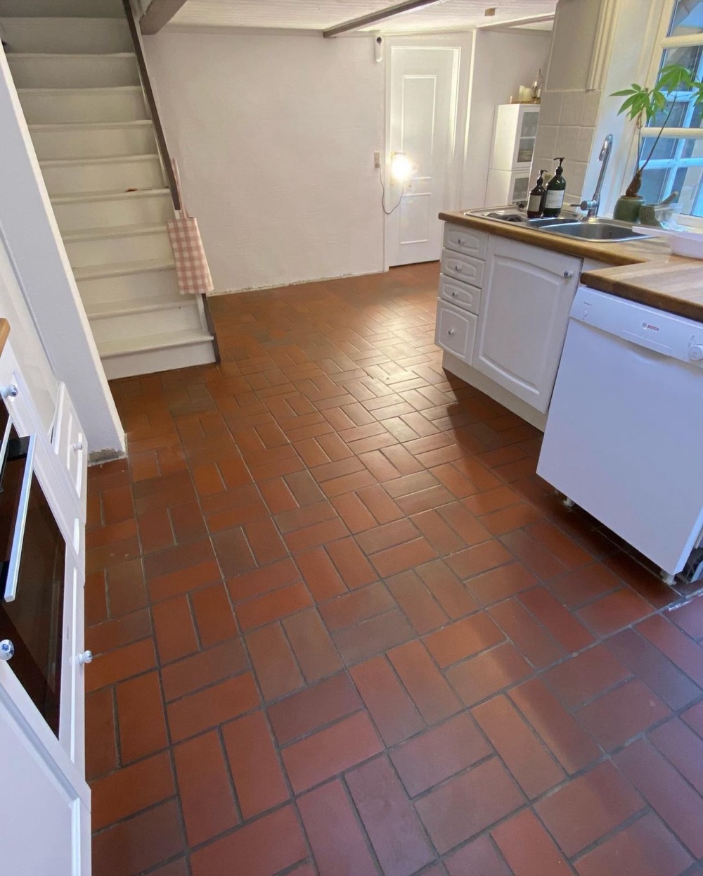 Before: dated red quarry tile floor in a kitchen and stair landing, before a microcement overlay